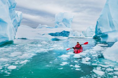 extreme tourism, winter kayaking in Antarctica, adventurous man paddling on sea kayak between icebergs clipart
