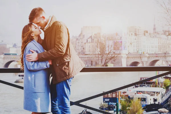 恋人同士パリの路上でキス新婚旅行でロマンチックな瞬間幸せな愛情に満ちた若い男と女セーヌ川の橋の上に立つ — ストック写真