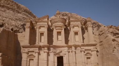A man climbing onto the roof of ancient ruins in Petra. Ad-Deir (The Monastery) is a monumental building carved out of rock in the ancient Jordanian city of Petra