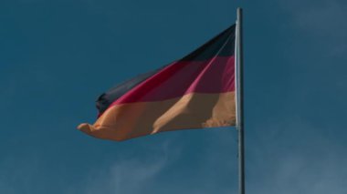 Avusturya ulusal bayrağı yavaş çekimde mavi bulutsuz gökyüzüne karşı dalgalanıyor.