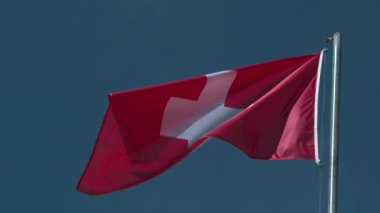 Avusturya ulusal bayrağı yavaş çekimde mavi bulutsuz gökyüzüne karşı dalgalanıyor.