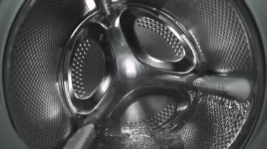 Çamaşır makinesi davulunun içinde renkli giysiler, dönüş döngüsü sırasında davulun yakın çekimi.