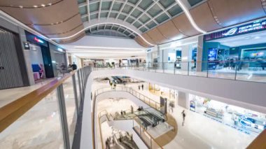 Alışveriş merkezinde alışveriş yapanlar, modern iç tasarımı gösteriyorlar, asansör ve yürüyen merdiven kullanan insanlar var.
