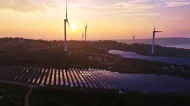 Kırsal kesimdeki güneş enerjisi panelleri ve rüzgar türbinlerinin günbatımı görüntüsü, yenilenebilir enerji kaynağı