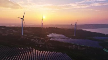 Kırsal bölgedeki güneş panelleri ve rüzgar türbinlerinin günbatımı görüntüsü, yenilenebilir enerji kaynağı