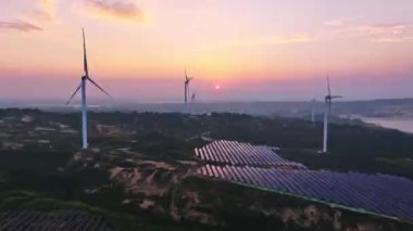 Kırsal bölgedeki güneş panelleri ve rüzgar türbinlerinin günbatımı görüntüsü, yenilenebilir enerji kaynağı