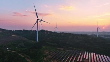 Kırsal bölgedeki güneş panelleri ve rüzgar türbinlerinin günbatımı görüntüsü, yenilenebilir enerji kaynağı