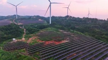 Kırsal bölgedeki güneş panelleri ve rüzgar türbinlerinin günbatımı görüntüsü, yenilenebilir enerji kaynağı