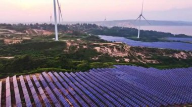 Kırsal bölgedeki güneş panelleri ve rüzgar türbinlerinin günbatımı görüntüsü, yenilenebilir enerji kaynağı