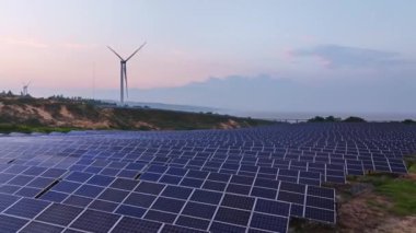 Kırsal kesimdeki güneş enerjisi panelleri ve rüzgar türbinlerinin günbatımı görüntüsü, yenilenebilir enerji kaynağı