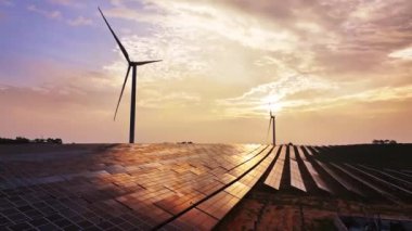Kırsal bölgedeki güneş panelleri ve rüzgar türbinlerinin günbatımı görüntüsü, yenilenebilir enerji kaynağı