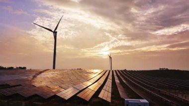 Kırsal bölgedeki güneş panelleri ve rüzgar türbinlerinin günbatımı görüntüsü, yenilenebilir enerji kaynağı