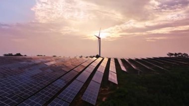 Kırsal kesimdeki güneş enerjisi panelleri ve rüzgar türbinlerinin günbatımı görüntüsü, yenilenebilir enerji kaynağı