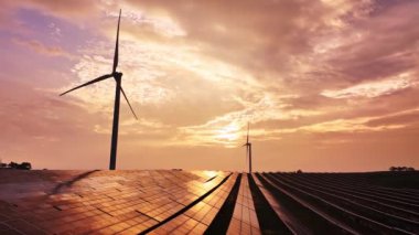 Kırsal bölgedeki güneş panelleri ve rüzgar türbinlerinin günbatımı görüntüsü, yenilenebilir enerji kaynağı