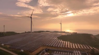 Kırsal bölgedeki güneş panelleri ve rüzgar türbinlerinin günbatımı görüntüsü, yenilenebilir enerji kaynağı