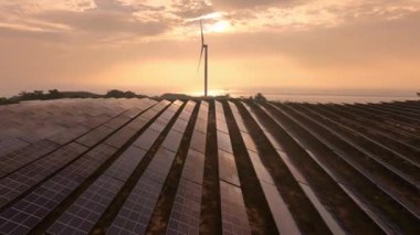 Kırsal bölgedeki güneş panelleri ve rüzgar türbinlerinin günbatımı görüntüsü, yenilenebilir enerji kaynağı