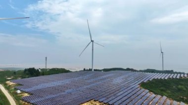 Kırsal kesimdeki güneş panelleri ve rüzgar türbinlerinin hava görüntüsü, yenilenebilir enerji kaynağı