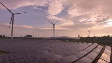 Kırsal bölgedeki güneş panelleri ve rüzgar türbinlerinin günbatımı görüntüsü, yenilenebilir enerji kaynağı