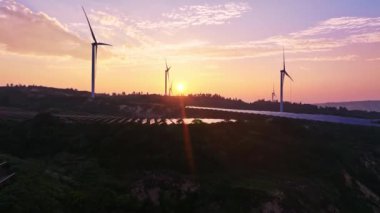 Kırsal bölgedeki güneş panelleri ve rüzgar türbinlerinin günbatımı görüntüsü, yenilenebilir enerji kaynağı