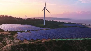 Kırsal kesimdeki güneş enerjisi panelleri ve rüzgar türbinlerinin günbatımı görüntüsü, yenilenebilir enerji kaynağı