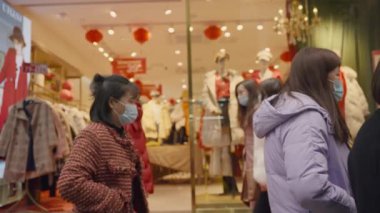 Sağlık maskesi takan Asyalılar elbise mağazasında yürüyorlar.