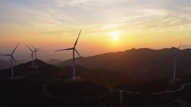 Rüzgar türbinleri gün batımında dağlardaki rüzgar enerji istasyonunda dönüyorlar..