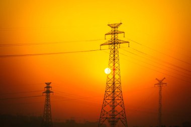 Günbatımının arka planında yüksek voltajlı elektrik hatları.