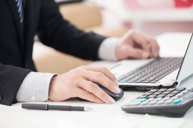 İşadamlarının elleri masanın üzerinde dizüstü bilgisayar ve kalemle çalışıyor.