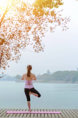 Göl kenarındaki iskelede yoga yapan genç bir kadın. 