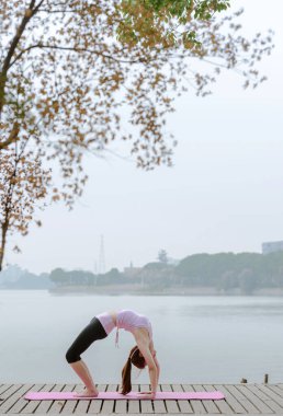 Göl kenarındaki iskelede yoga yapan genç bir kadın. 