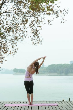 Göl kenarındaki iskelede yoga yapan genç bir kadın. 