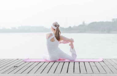 Göl kenarındaki iskelede yoga yapan genç bir kadın. 