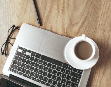 Tahta masadaki dizüstü bilgisayarda bir fincan kahve.