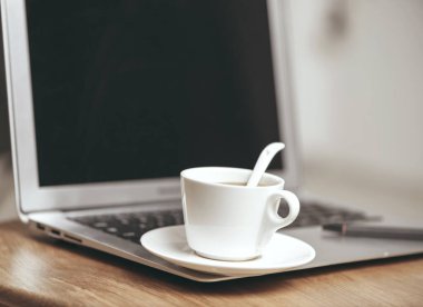 Laptop ve bir fincan kahve tahta masada. 