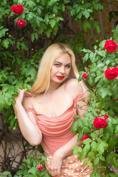 금발의 머리와 입술을 아름다운 정원에서 꽃피는 장미꽃 근처에 모습을 드러낸다 — 스톡 사진