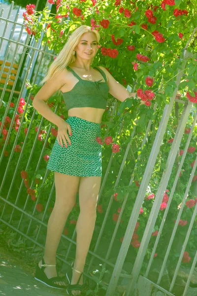 ブロンドの髪をした愛らしい女性が庭でポーズ 緑のスカートとTシャツでCucasian嬉しい女の子の肖像とともにバラ — ストック写真