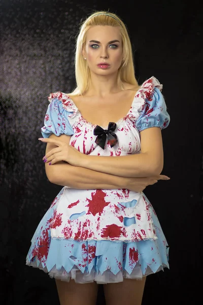 Beautiful young blonde woman in an Alice costume. The dress is torn and stained with fake blood. Halloween concept. Soft focus