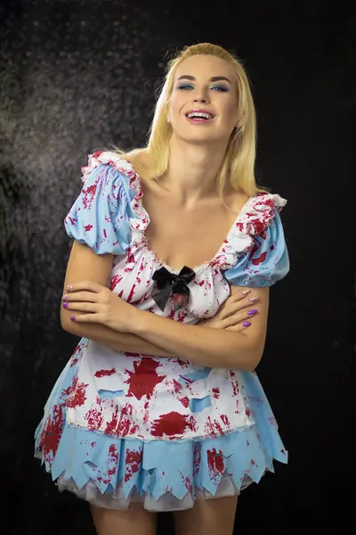 Beautiful young blonde woman in an Alice costume. The dress is torn and stained with fake blood. Halloween concept. Soft focus
