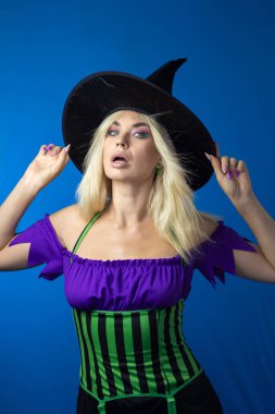 Mavi arka planda cadı kostümlü güzel sarışın kadın. Kısa elbise, uzun saç, siyah şapka. Cadılar Bayramı konsepti Yumuşak odak