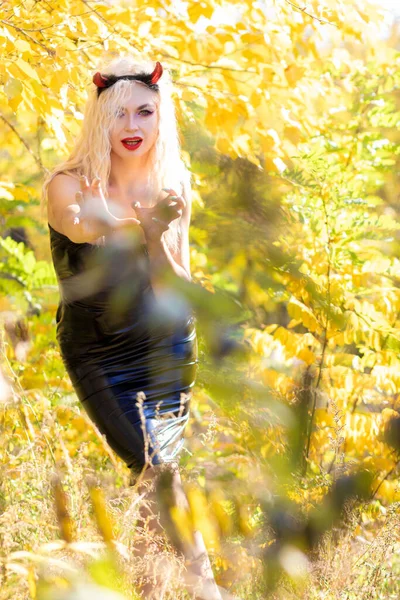 美しい金髪の女性は 自然の中で悪魔の衣装を着ています ブラックラテックスタイトなドレスとホーン ソフトフォーカス ハロウィーンコンセプト — ストック写真