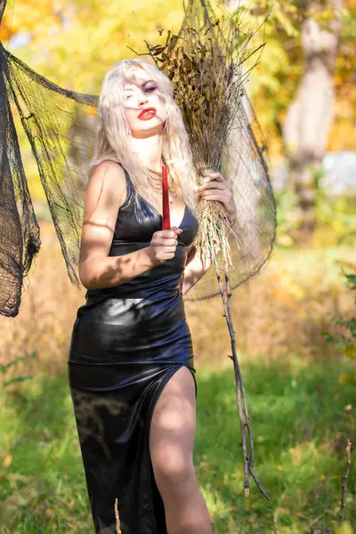 一个金发碧眼的女巫师的照片 一件长长的皮衣 手里拿着一把扫帚 万圣节的概念 — 图库照片