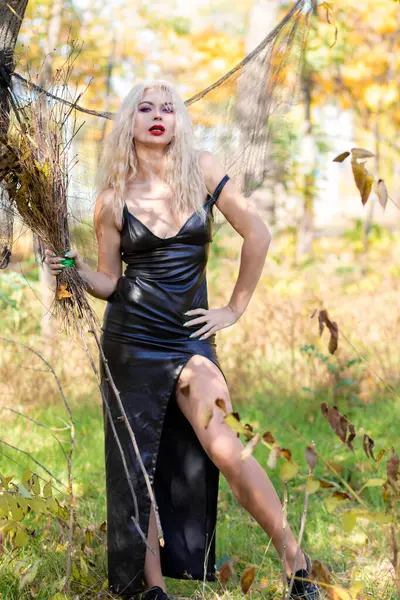 魔女のイメージに重い髪のブロンドの写真撮影 長い革のドレスと彼女の手のブロム ハロウィーンコンセプト — ストック写真