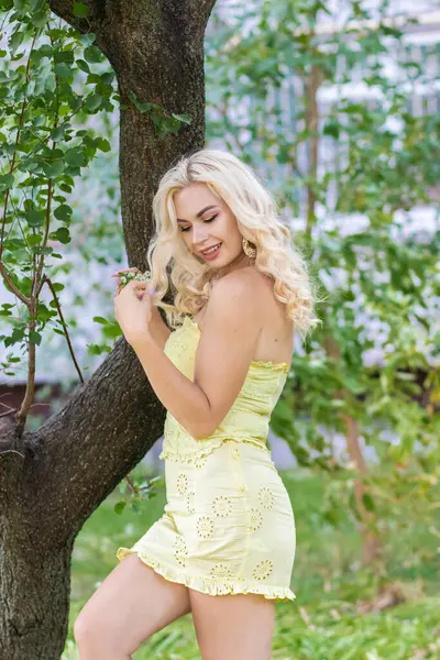 Sarı dantelli bir takım elbiseli, ağacın yanında eteği olan güzel, gülümseyen sarışın kadın..