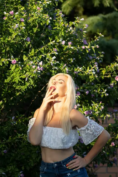 Yeşil bitkilerin arka planında kısa kollu ve kot şortlu dantelli beyaz bir kadının portresi.