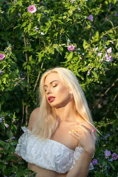 Yeşil bitkilerin arka planında kısa kollu ve kot şortlu dantelli beyaz bir kadının portresi.