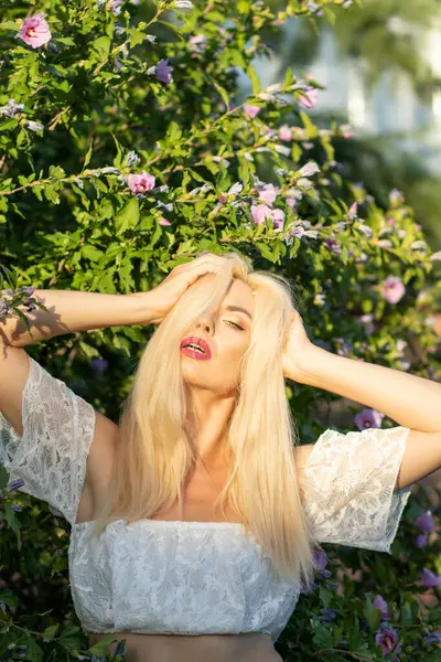 Yeşil bitkilerin arka planında kısa kollu ve kot şortlu dantelli beyaz bir kadının portresi.