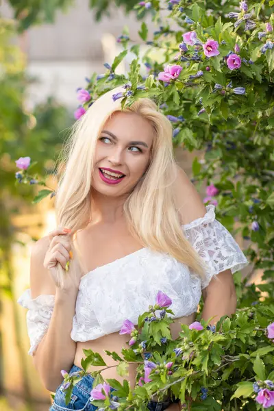 Yeşil bitkilerin arka planında kısa kollu ve kot şortlu dantelli beyaz bir kadının portresi.