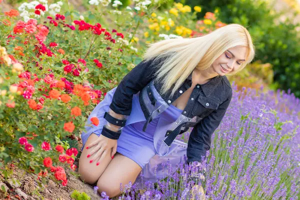 Leylak rengi bir elbisenin içinde uzun saçlı ve doğal makyajlı bir sarışının portresi lavanta çiçeklerinin arasında bir tarlada duruyor. Yaz sabahı