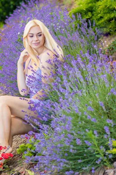 Leylak rengi bir elbisenin içinde uzun saçlı ve doğal makyajlı bir sarışının portresi lavanta çiçeklerinin arasında bir tarlada duruyor. Yaz sabahı