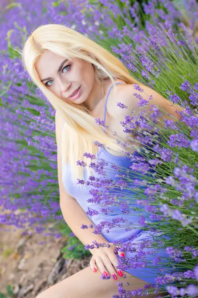 Leylak rengi bir elbisenin içinde uzun saçlı ve doğal makyajlı bir sarışının portresi lavanta çiçeklerinin arasında bir tarlada duruyor. Yaz sabahı